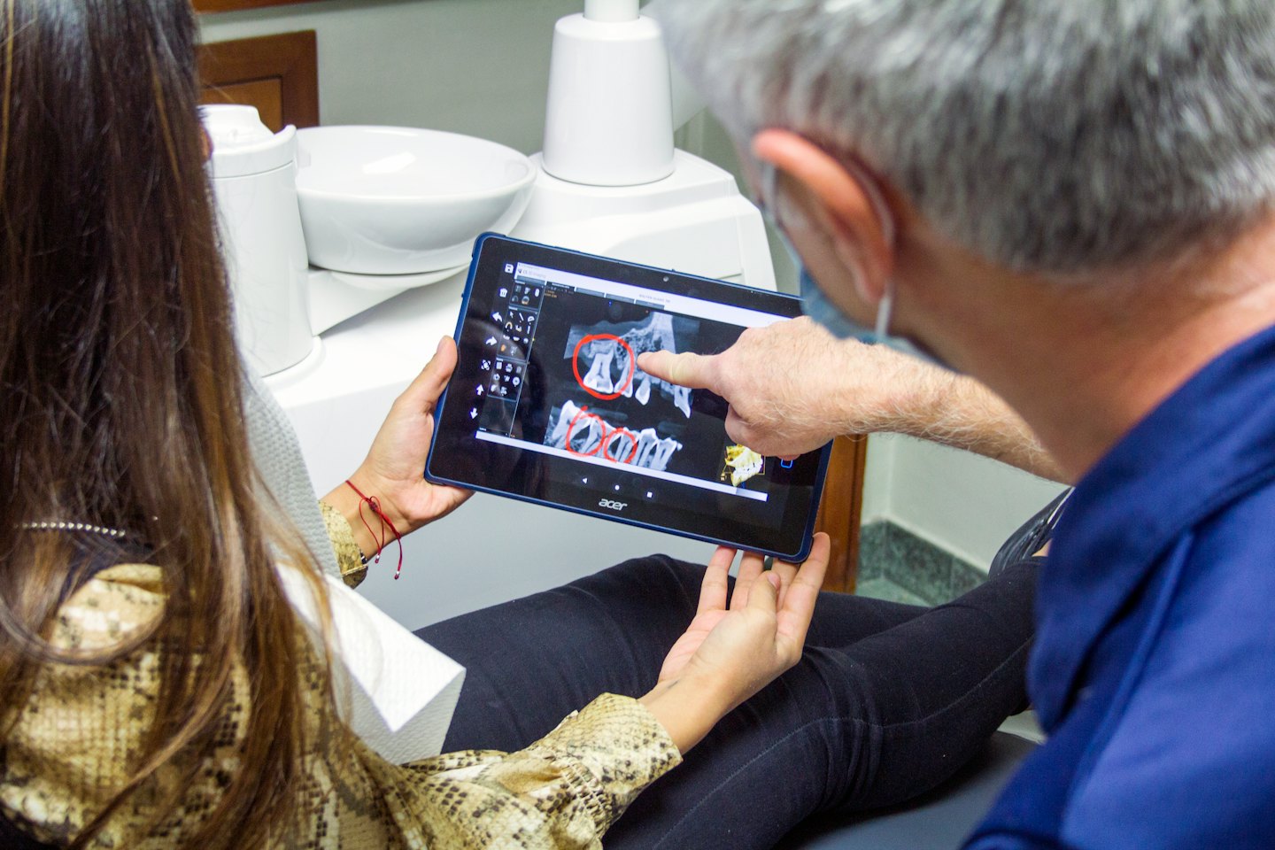 Dentist showing patient dental X-ray on tablet.